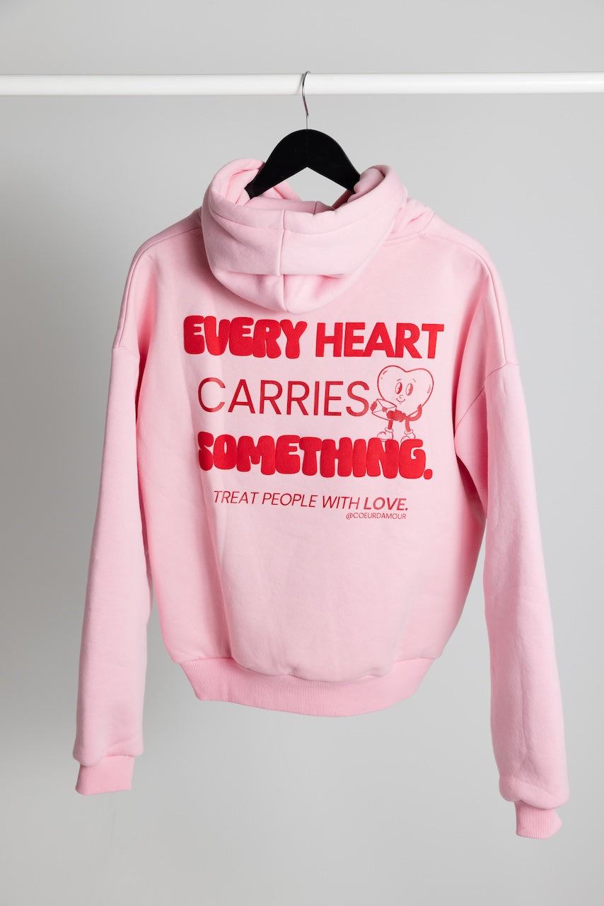 Oversize Hoodie mit rotem Backprint "Every Heart carries something" hängt an einem Kleiderbügel vor neutralem Hintergrund.