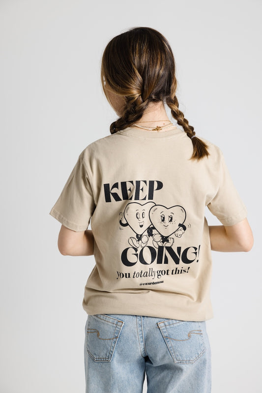 Frau von hinten mit Zöpfen trägt ein beiges Oversize T-Shirt mit schwarzem "KEEP GOING! you totally got this" Backprint. Dazu eine hellblaue Jeans vor neutralem Hintergrund
