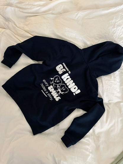 Hoodie liegt auf einem weißen Laken auf dem Boden, weißer Backprint "remember to BE KIND! every SMILE hides a story"