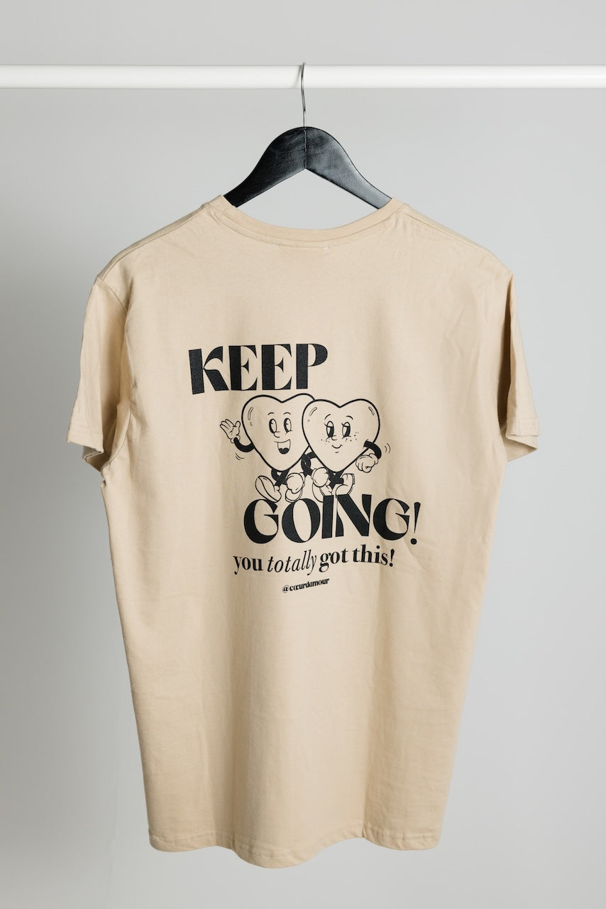beiges Oversize T-Shirt mit schwarzem "KEEP GOING! you totally got this" Backprint, hängt an einem Kleiderbügel vor neutralem Hintergrund.