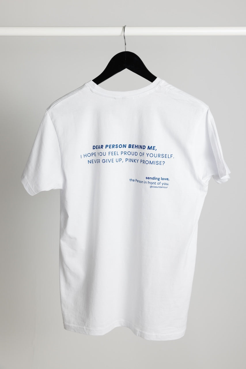 weißes Shirt mit dunkelblauem Aufdruck "Dear Person behind me, i hope you feel proud of yourself, never give up, pinky promise?" hängend an einem Kleiderbügel vor neutralem Hintergrund.