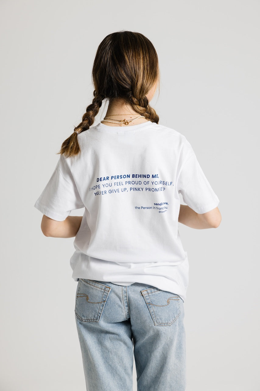 Frau von hinten mit Zöpfen trägt ein weißes Shirt mit dunkelblauem Aufdruck "Dear Person behind me, i hope you feel proud of yourself, never give up, pinky promise?". Dazu eine hellblaue Jeans.