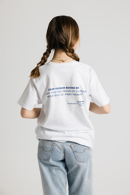 Frau von hinten mit Zöpfen trägt ein weißes Shirt mit dunkelblauem Aufdruck "Dear Person behind me, i hope you feel proud of yourself, never give up, pinky promise?". Dazu eine hellblaue Jeans.
